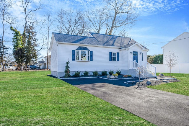 view of front of home featuring driveway, roof with shingles, fence, and a front yard