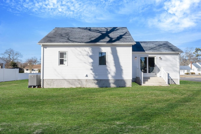 back of house with a shingled roof, entry steps, a lawn, and fence