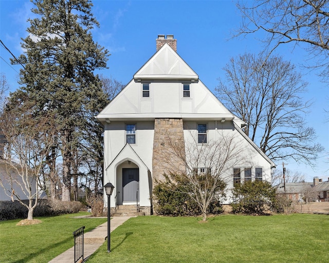 view of front of house with stucco siding, a chimney, and a front lawn