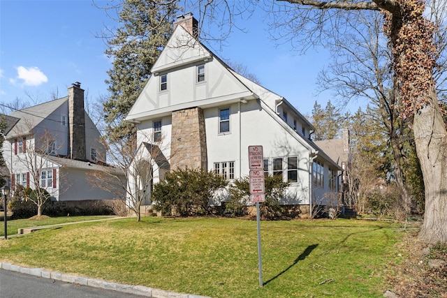 tudor-style house featuring stucco siding, a chimney, and a front yard