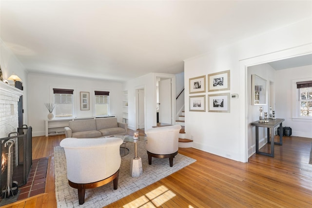 living room with stairway, baseboards, light wood-style floors, and a brick fireplace