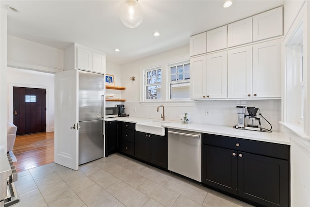 kitchen featuring decorative backsplash, appliances with stainless steel finishes, dark cabinetry, white cabinets, and a sink