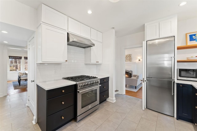 kitchen featuring tasteful backsplash, under cabinet range hood, high quality appliances, light countertops, and white cabinetry