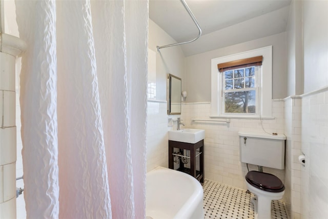 full bathroom with a tub to relax in, a wainscoted wall, a sink, tile patterned flooring, and tile walls