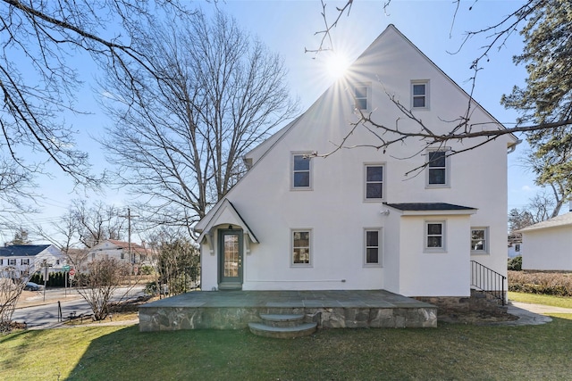 rear view of property featuring a patio, a lawn, and stucco siding