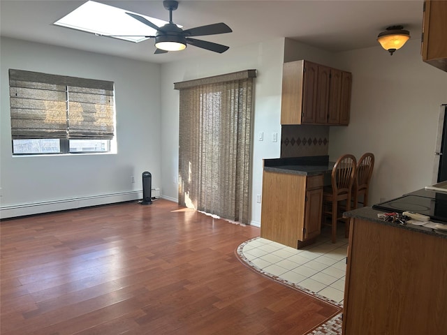 kitchen with dark countertops, a baseboard heating unit, light wood-style flooring, brown cabinetry, and a ceiling fan