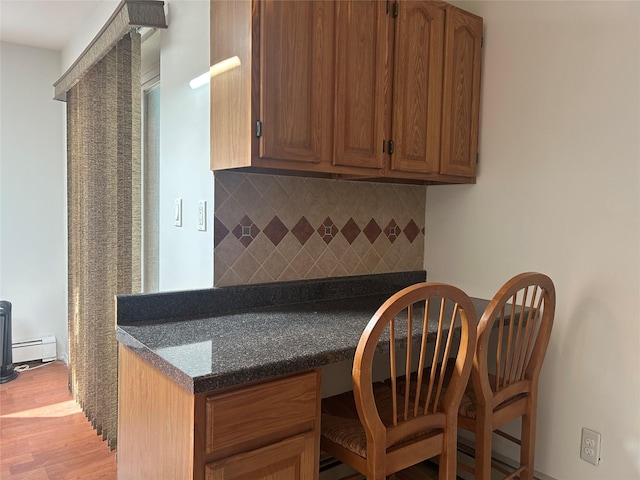 kitchen featuring light wood-type flooring, tasteful backsplash, built in desk, brown cabinetry, and a baseboard radiator