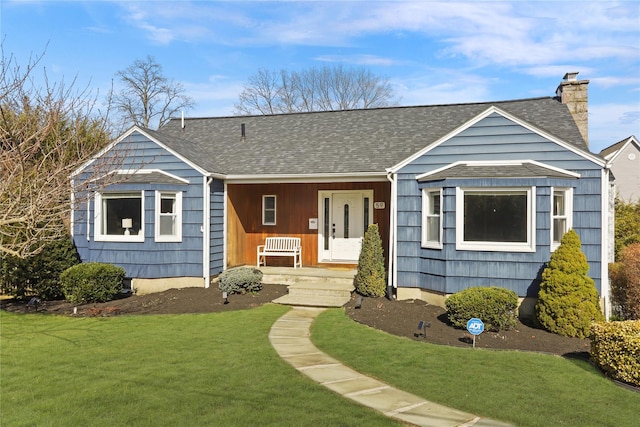 view of front of home featuring a front yard, covered porch, a chimney, and a shingled roof