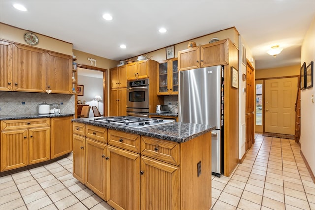 kitchen with light tile patterned floors, a kitchen island, glass insert cabinets, appliances with stainless steel finishes, and tasteful backsplash