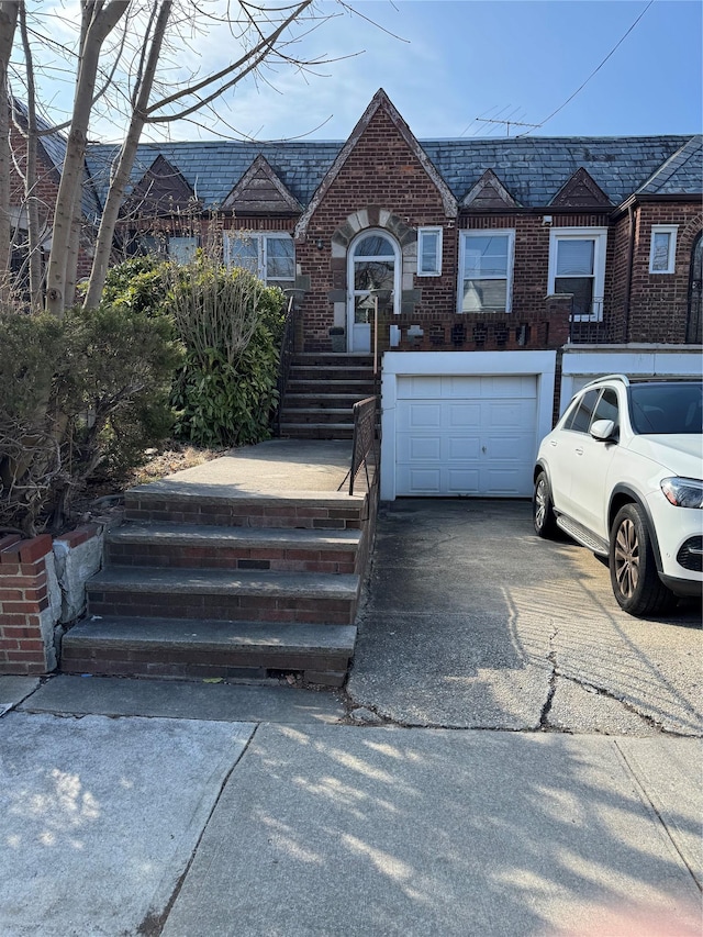 view of front of home featuring driveway, brick siding, an attached garage, and a high end roof