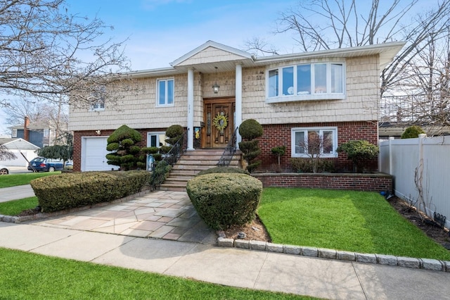 bi-level home with driveway, fence, a front yard, a garage, and brick siding