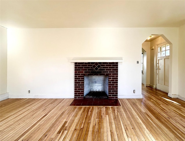 unfurnished living room featuring arched walkways, wood-type flooring, a fireplace, and baseboards