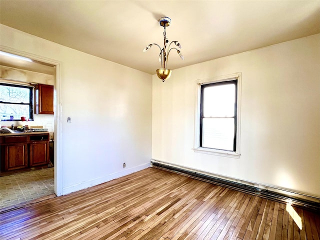 spare room with a chandelier, light wood-style flooring, and baseboards