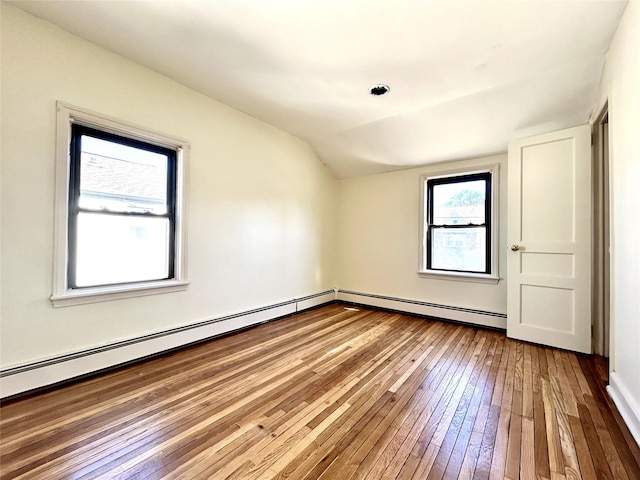 empty room featuring lofted ceiling, baseboard heating, and hardwood / wood-style flooring