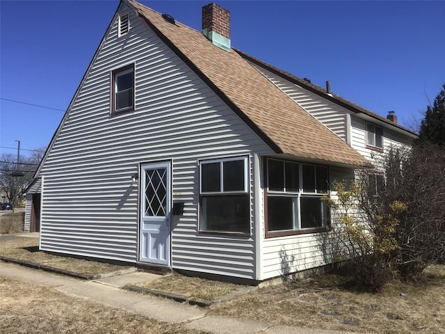 view of side of home with roof with shingles and a chimney