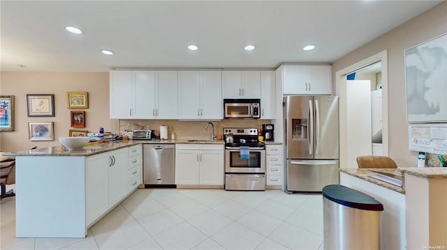 kitchen with stainless steel appliances, stone counters, a sink, and a peninsula