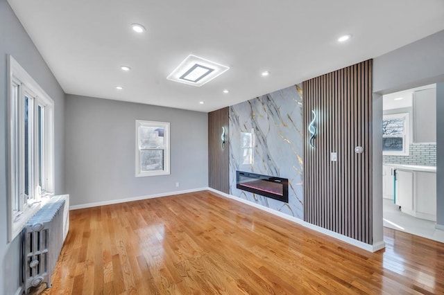 unfurnished living room with a high end fireplace, radiator, baseboards, light wood-type flooring, and recessed lighting