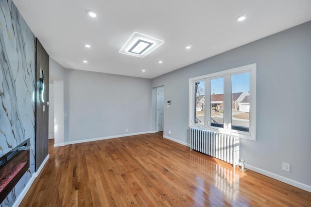 unfurnished living room featuring radiator heating unit, wood finished floors, recessed lighting, and baseboards