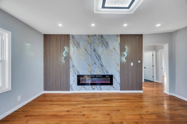 unfurnished living room with wood finished floors, baseboards, recessed lighting, a high end fireplace, and an accent wall