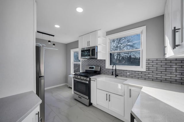 kitchen with marble finish floor, radiator heating unit, white cabinetry, appliances with stainless steel finishes, and decorative backsplash