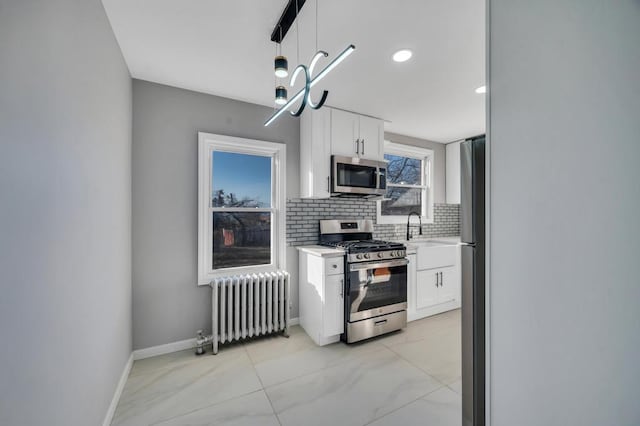 kitchen featuring radiator, stainless steel appliances, light countertops, white cabinetry, and backsplash