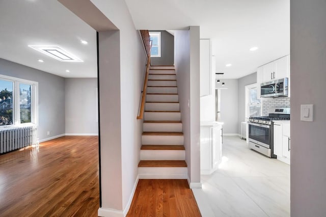 staircase featuring baseboards, radiator, a healthy amount of sunlight, and wood finished floors