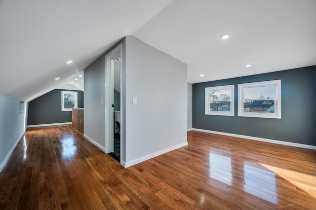 additional living space featuring baseboards, lofted ceiling, hardwood / wood-style floors, and a healthy amount of sunlight