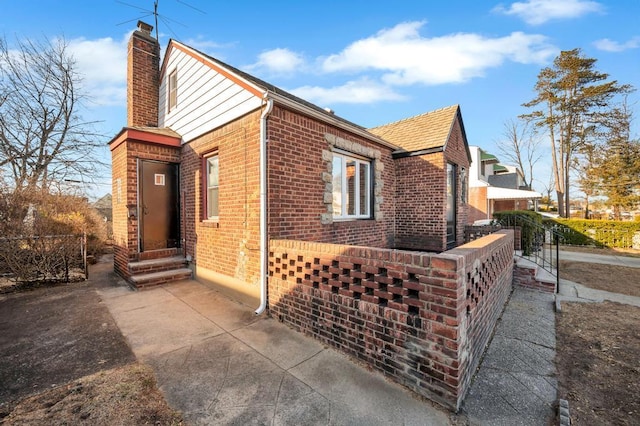 view of side of home featuring entry steps, fence, brick siding, and a chimney