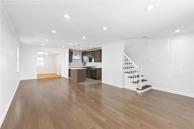 unfurnished living room featuring recessed lighting, stairway, wood finished floors, and ornamental molding