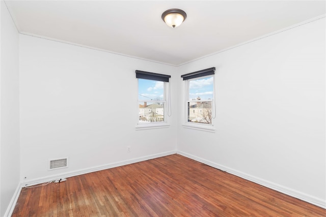 empty room featuring ornamental molding, wood finished floors, visible vents, and baseboards