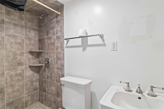 bathroom featuring toilet, a tile shower, and a sink