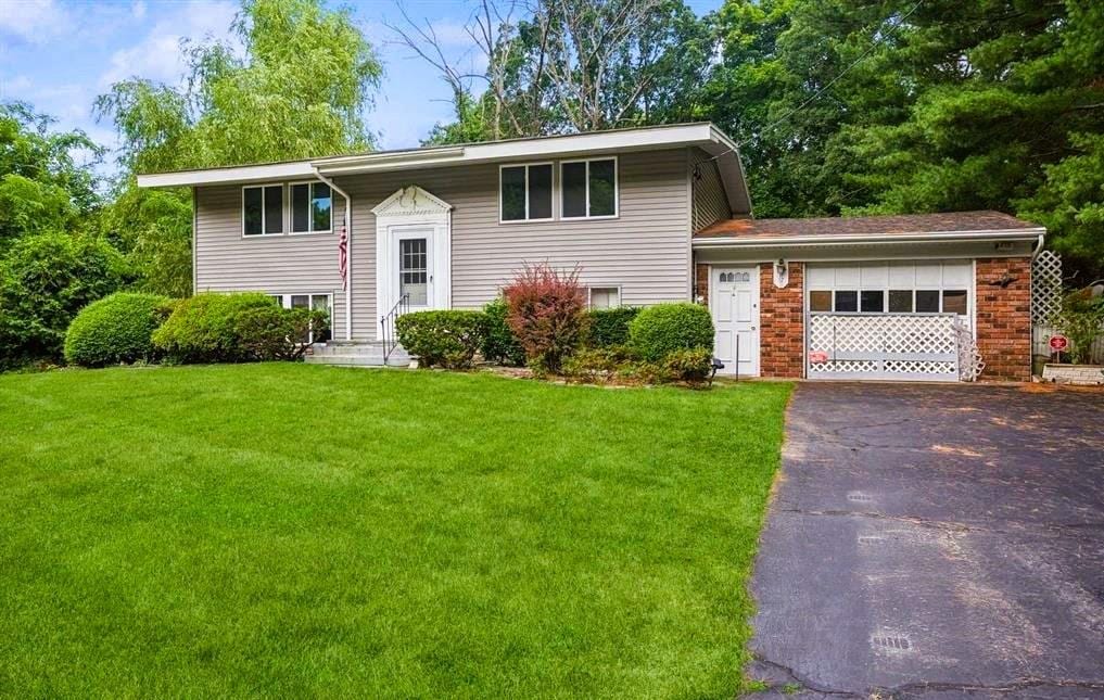 split foyer home with a front lawn, an attached garage, brick siding, and driveway