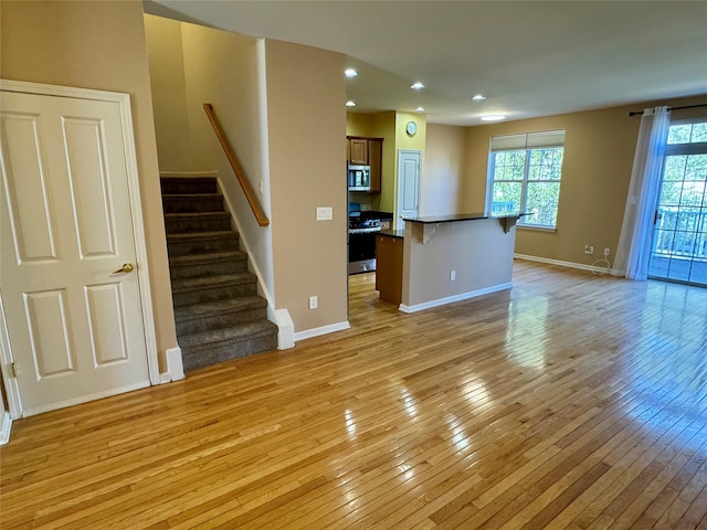 unfurnished living room with stairway, light wood-style floors, and baseboards