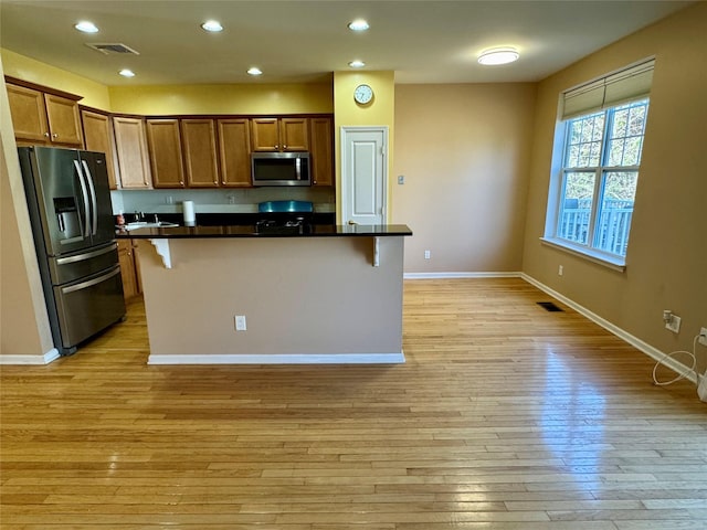 kitchen with dark countertops, stainless steel microwave, light wood-type flooring, refrigerator with ice dispenser, and a kitchen breakfast bar