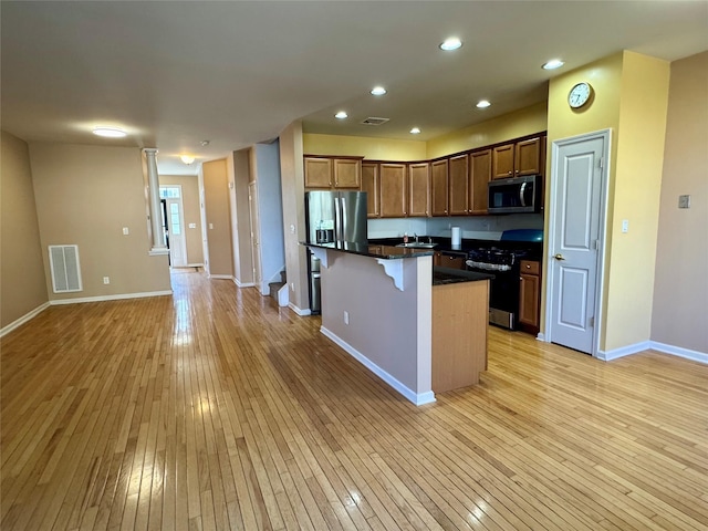 kitchen featuring visible vents, light wood finished floors, a kitchen island, stainless steel appliances, and a kitchen bar