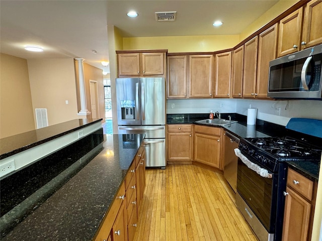 kitchen featuring visible vents, a sink, stainless steel appliances, light wood-style floors, and decorative columns