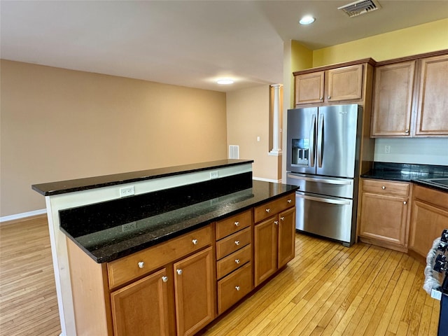 kitchen featuring visible vents, light wood finished floors, dark stone counters, stainless steel refrigerator with ice dispenser, and a center island