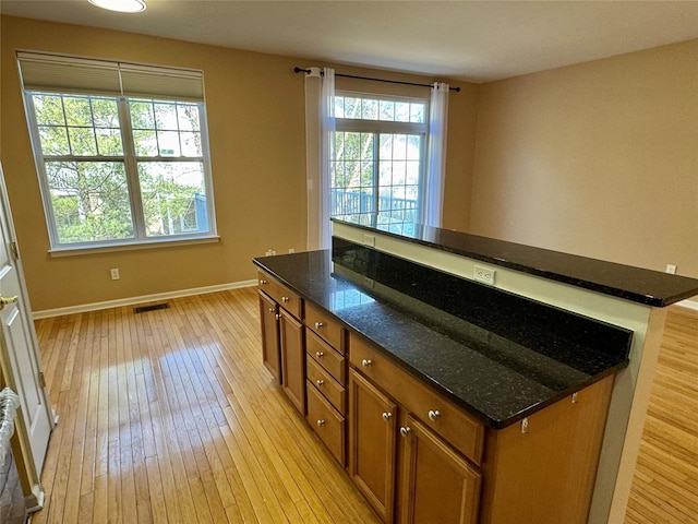 kitchen featuring light wood-type flooring, visible vents, dark stone countertops, a center island, and brown cabinetry