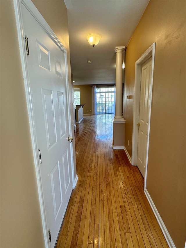 hall featuring hardwood / wood-style flooring, decorative columns, and baseboards