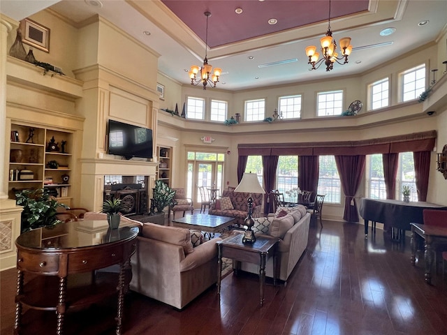 living area with dark wood finished floors, an inviting chandelier, a tray ceiling, and ornamental molding