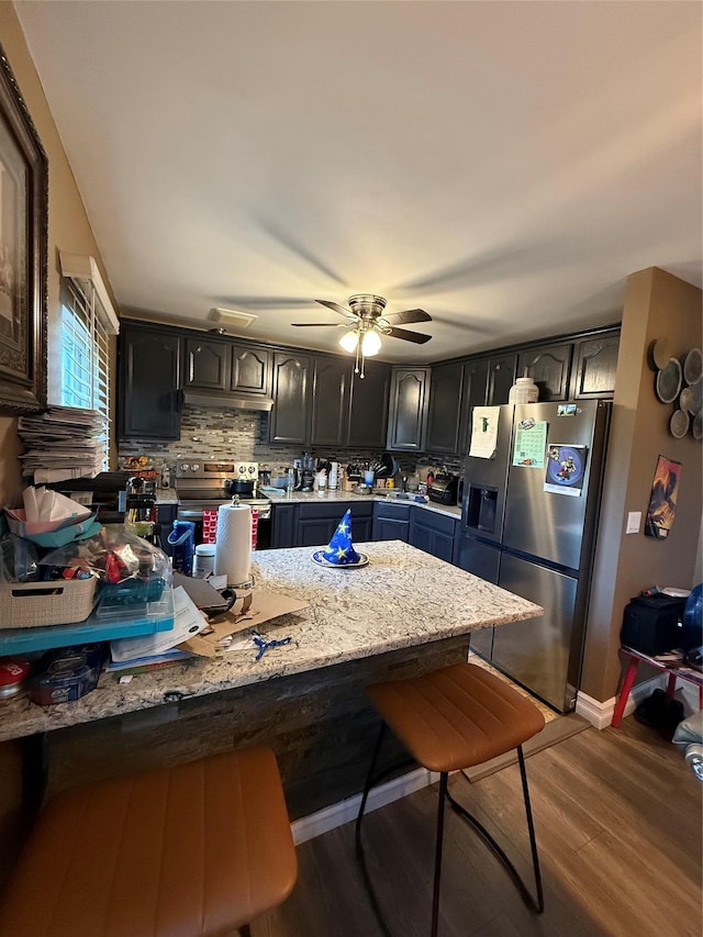 kitchen with stainless steel appliances, a breakfast bar, a peninsula, light wood-type flooring, and decorative backsplash