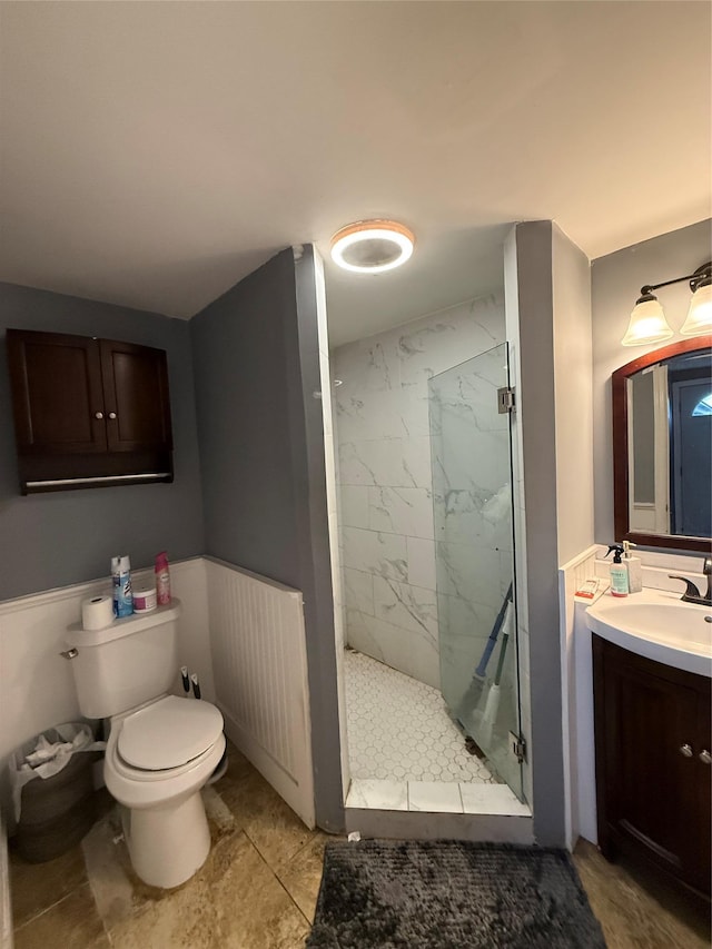 bathroom featuring toilet, a wainscoted wall, a marble finish shower, and vanity