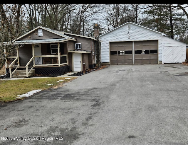 view of front of home with a detached garage, covered porch, an outdoor structure, and a chimney