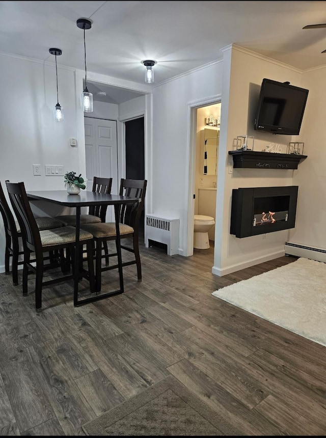 dining room with radiator, crown molding, dark wood-style flooring, a warm lit fireplace, and a baseboard radiator