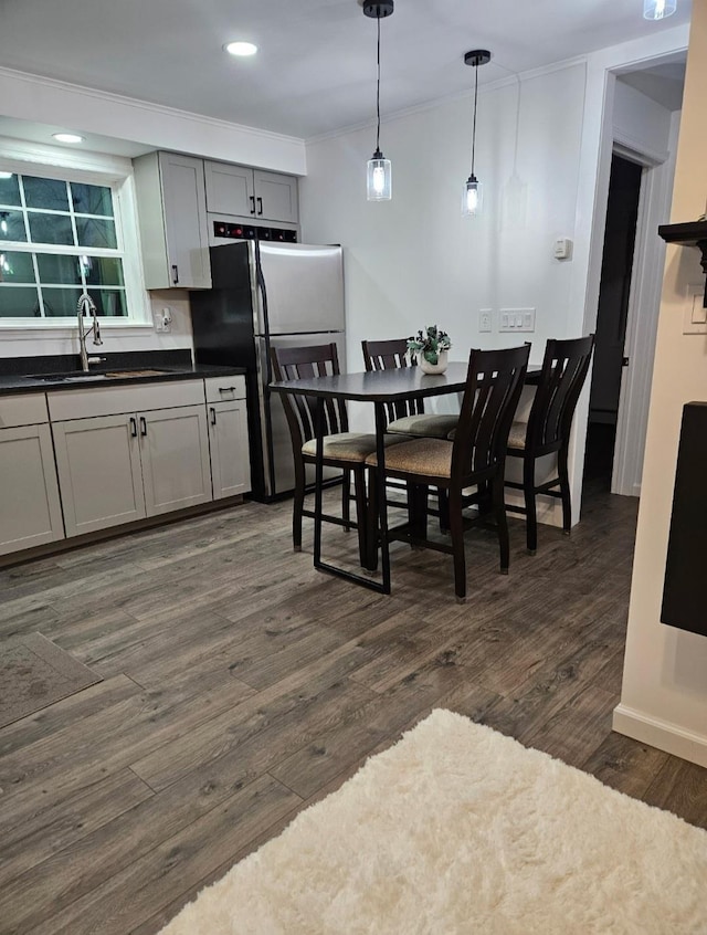 kitchen with dark countertops, a sink, crown molding, freestanding refrigerator, and dark wood-style flooring