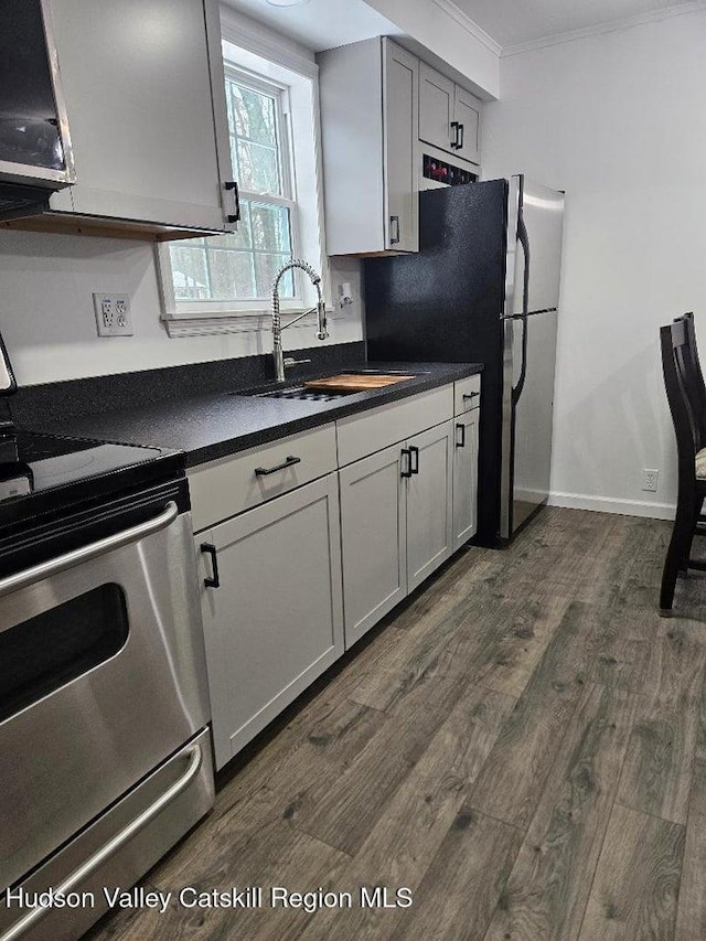 kitchen featuring dark wood-style floors, ornamental molding, a sink, stove, and dark countertops