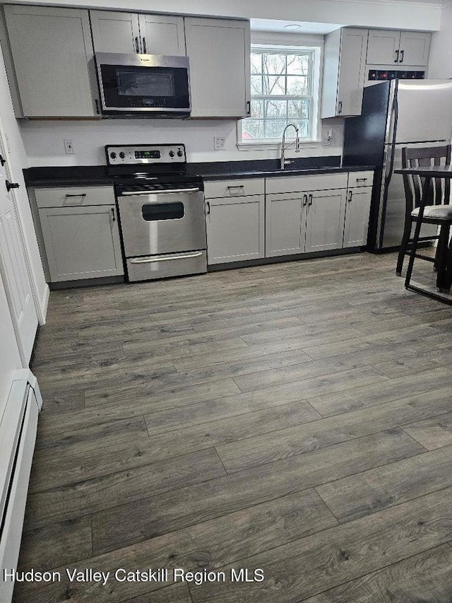 kitchen with dark countertops, a baseboard radiator, dark wood-style flooring, appliances with stainless steel finishes, and a sink