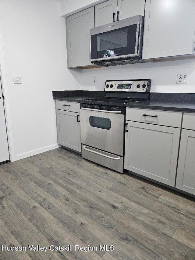 kitchen with dark countertops, stainless steel appliances, baseboards, and wood finished floors