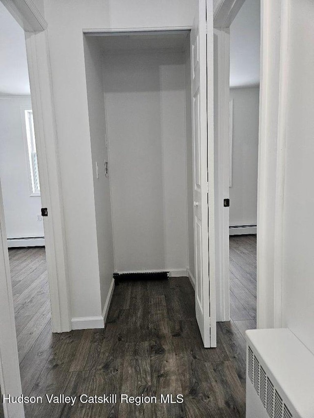 corridor with dark wood-type flooring, baseboards, and baseboard heating