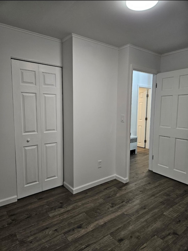 unfurnished bedroom featuring a closet, baseboards, dark wood finished floors, and crown molding